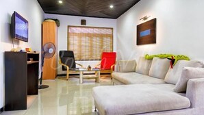 A modern living room with a sofa, a red chair, a wooden cabinet, a television, and a large window with blinds. - Grand Conch Villa (Tangalle)