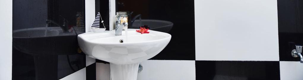 Ett badrum med ett vitt handfat, svartvita kakelväggar och en spegel.