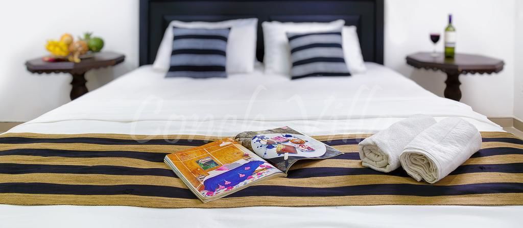 Een net opgemaakt bed met een gestreept dekbedovertrek, een gevouwen handdoek en een reisblad.