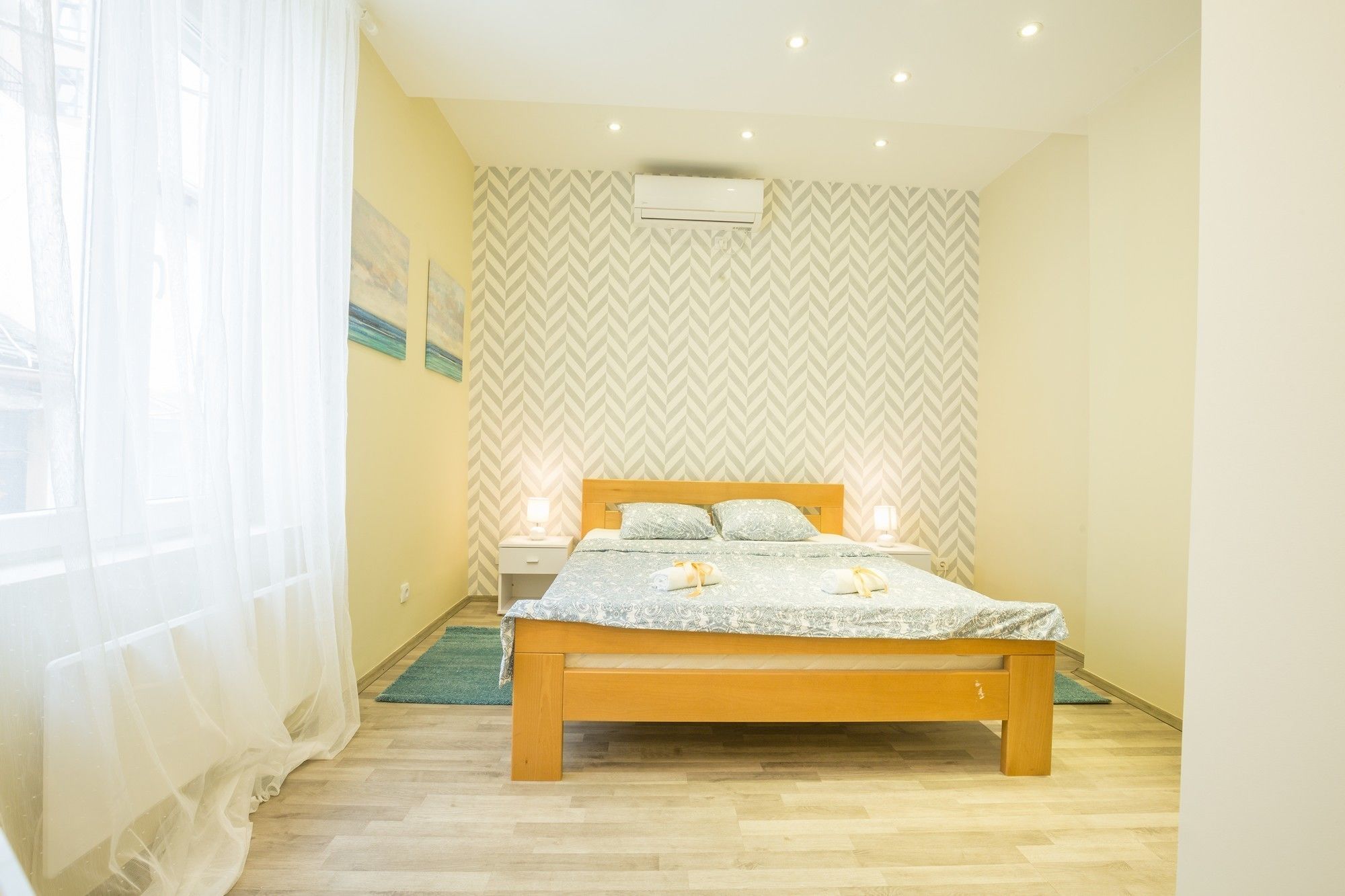 Un dormitorio con una cama de madera, dos mesitas de noche, aire acondicionado instalado en la pared y papel tapiz estampado.