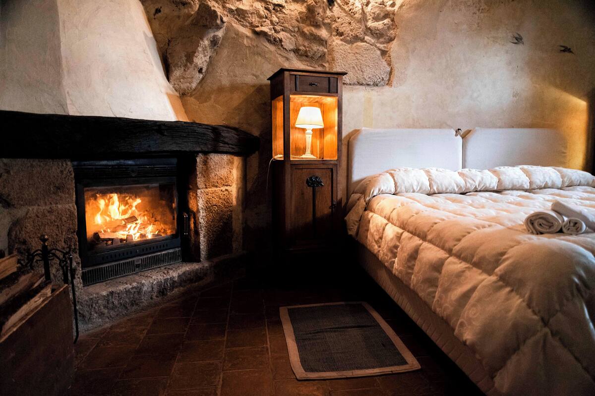 A cozy room with a stone fireplace, a bed with a white duvet, and a nightstand with a lamp.
