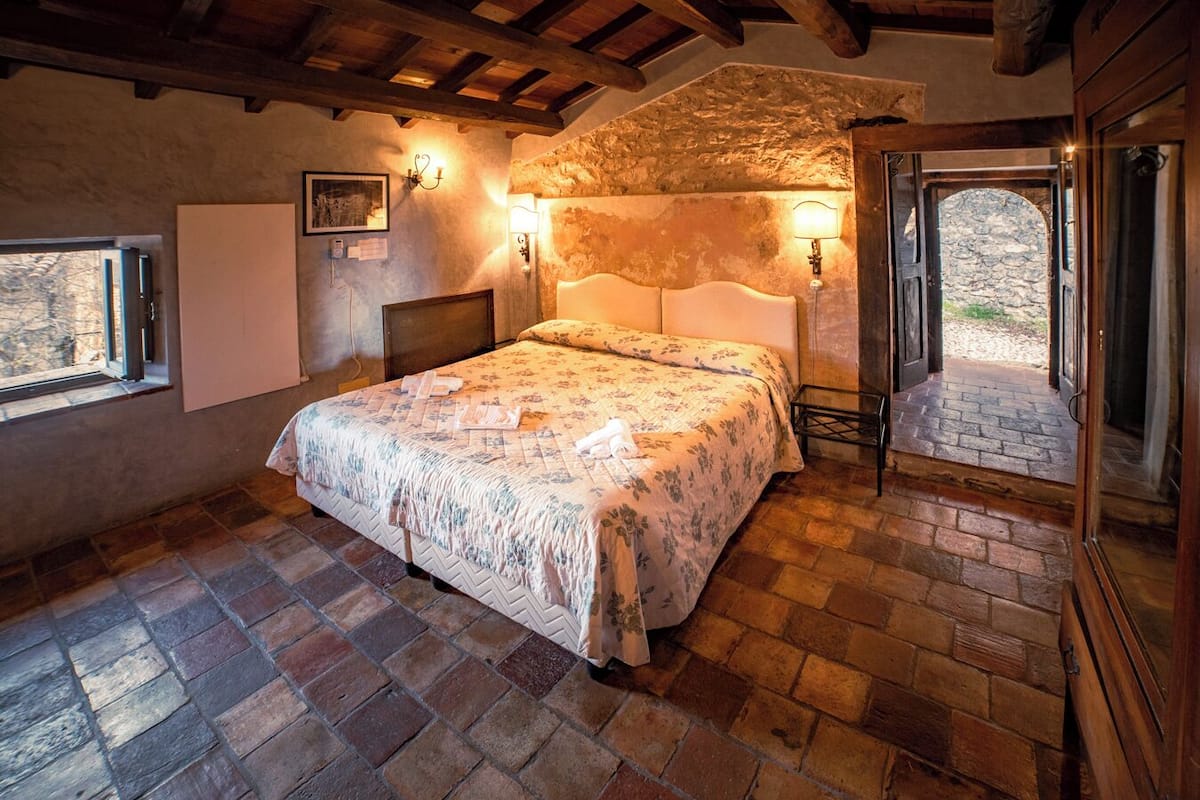 A bedroom with a bed, stone walls, a wooden ceiling, and a stone floor.