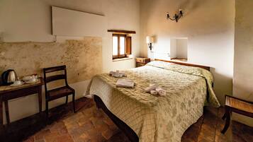 A bedroom with a bed, a chair, a table with a kettle, and a window.