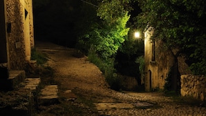 Un camino adoquinado que lleva a un edificio de piedra, con una fuente de luz iluminando el entorno.