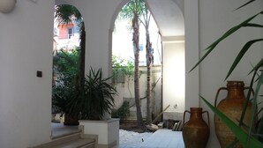 A courtyard with tiled flooring, a palm tree, and large vases.