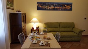 A dining area with a table set for breakfast, a green sofa, a lamp, and a cityscape painting on the wall.