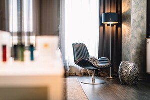 Una habitación moderna con un sillón de cuero oscuro, una lámpara de pie y un jarrón texturizado sobre un piso de madera.
