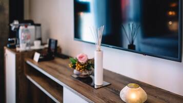 Un comptoir d’accueil en bois, avec une machine à café, un vase contenant une fleur rose et une bougie allumée.