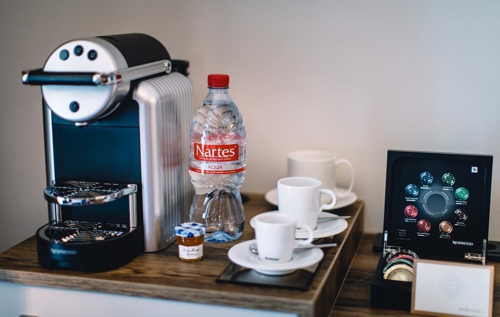 A coffee machine, a bottle of water, and a display of coffee flavors on a wooden table.