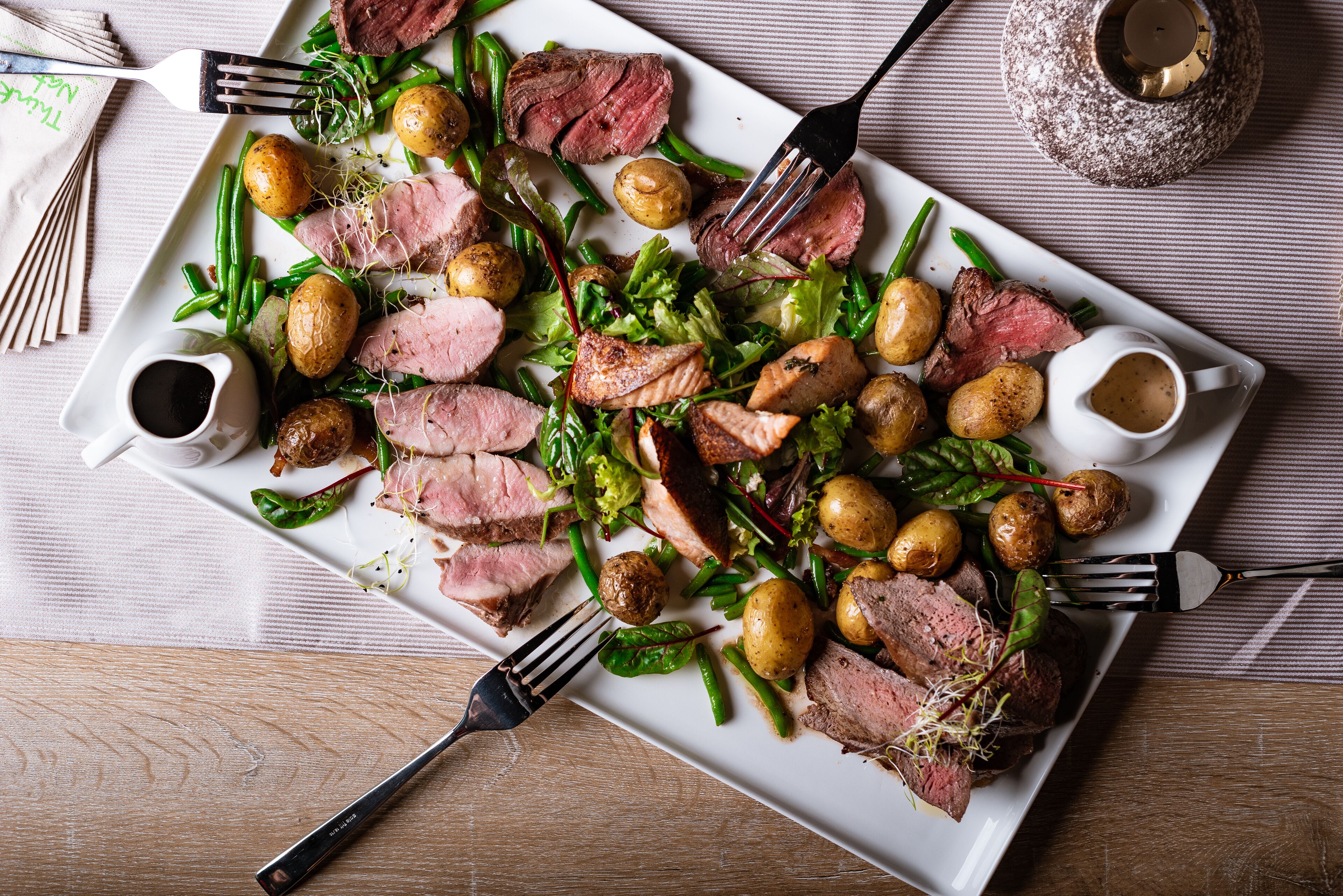 A plate of sliced meat, potatoes, and greens on a rectangular white plate.