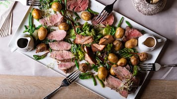 A plate of sliced meat, potatoes, and greens on a rectangular white plate.