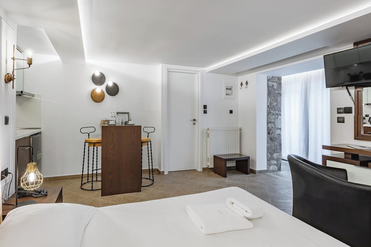 Ein Hotelzimmer mit Bett, Schreibtisch mit Stuhl, Nachttisch mit Lampe und Fernseher.