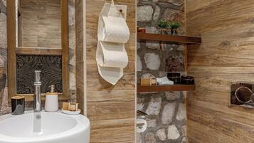 Un baño con un lavamanos grande, inodoro y espejo. Hay estantes con artículos de aseo y un perchero para toallas.