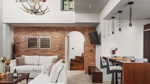 A modern living room with a white sofa, a dining area with a wooden table, and a brick wall. - Vintage Suites Trikala (Trikala)