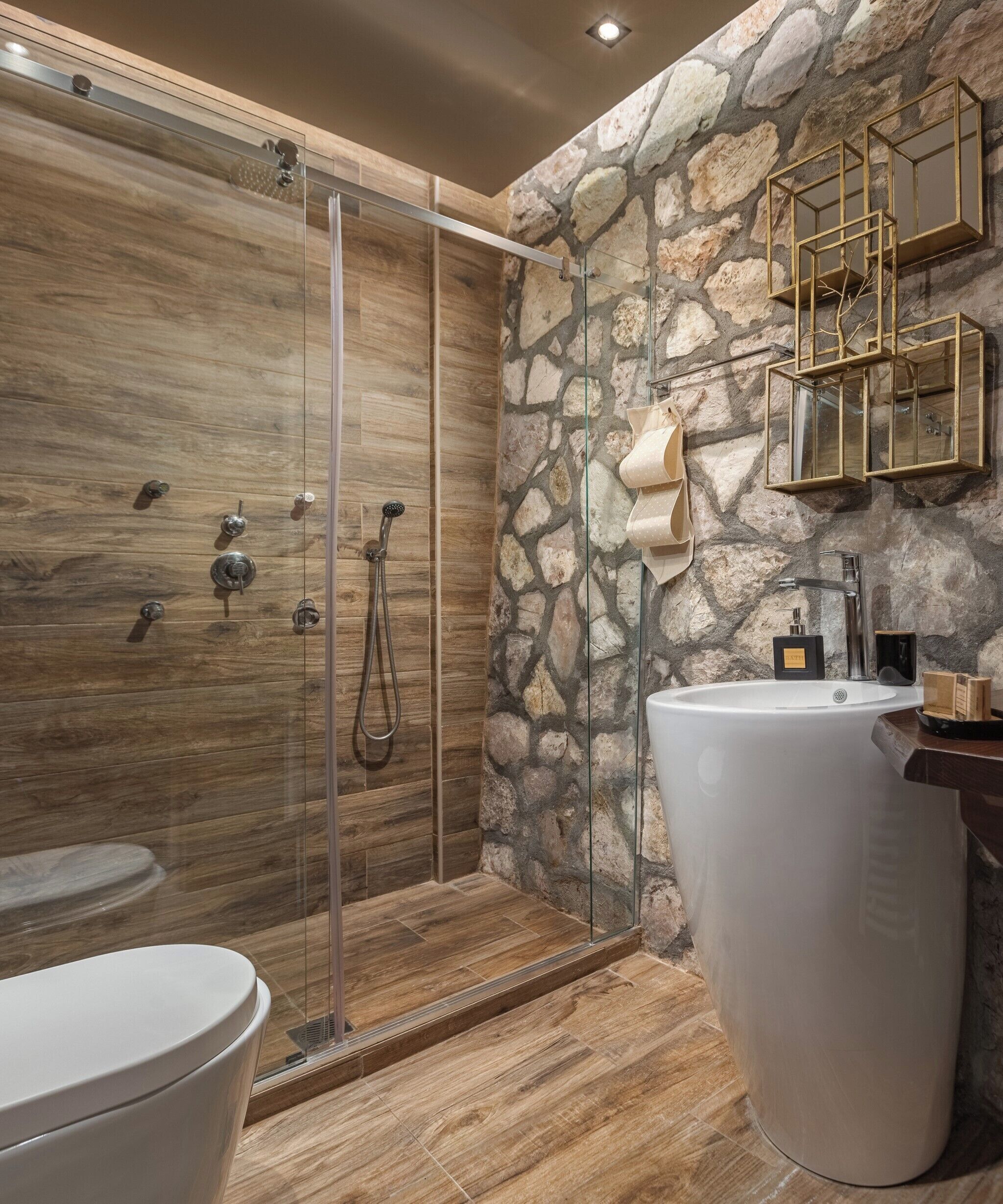 A modern bathroom with a glass-enclosed shower, a large white sink, and a stone wall backdrop.