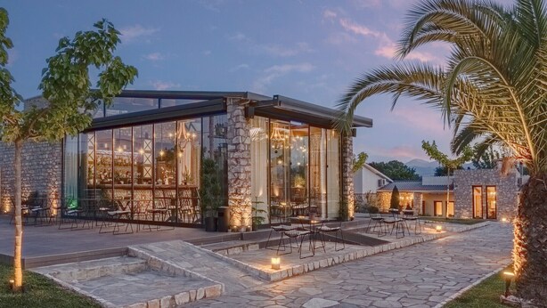 A modern building with large glass windows, stone walls, and outdoor seating. - Vintage Suites Trikala (Trikala)