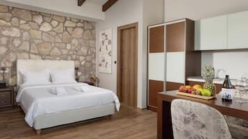 Un dormitorio con pared de piedra, cama con ropa de cama blanca, escritorio de madera con frutero, una silla y un minibar.