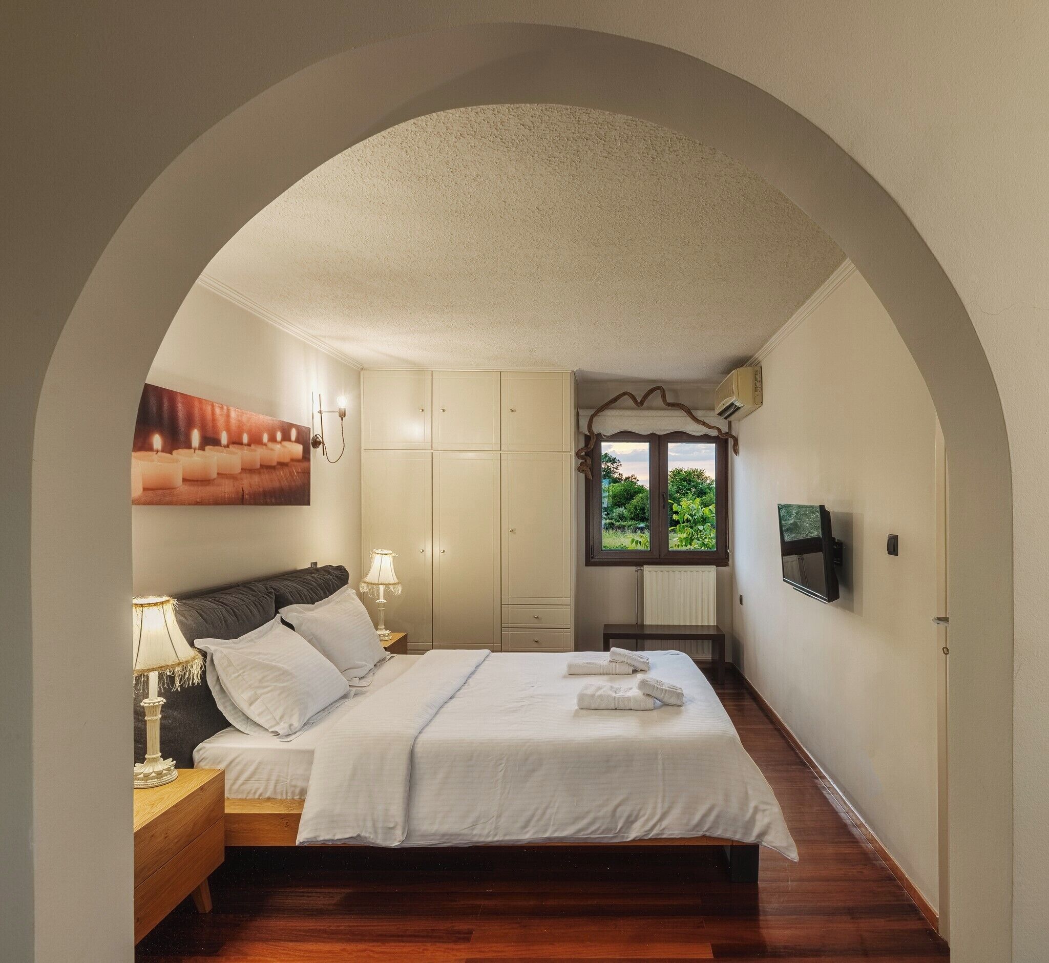Une chambre à coucher comprenant un lit, des tables de chevet, une armoire, un banc et un téléviseur fixé au mur.