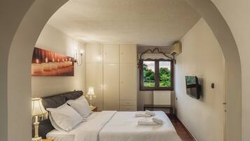 Une chambre à coucher comprenant un lit, des tables de chevet, une armoire, un banc et un téléviseur fixé au mur.