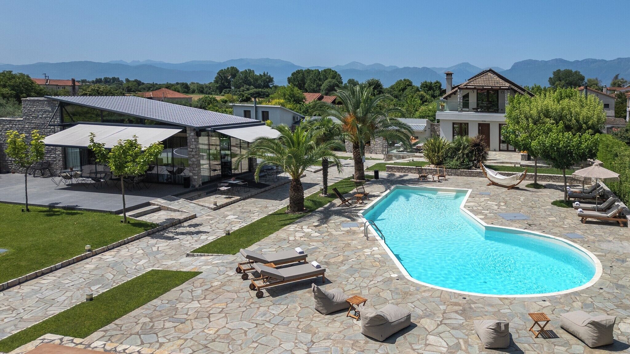Zona de piscina con sillones de descanso, un patio de piedra y vistas a montañas.