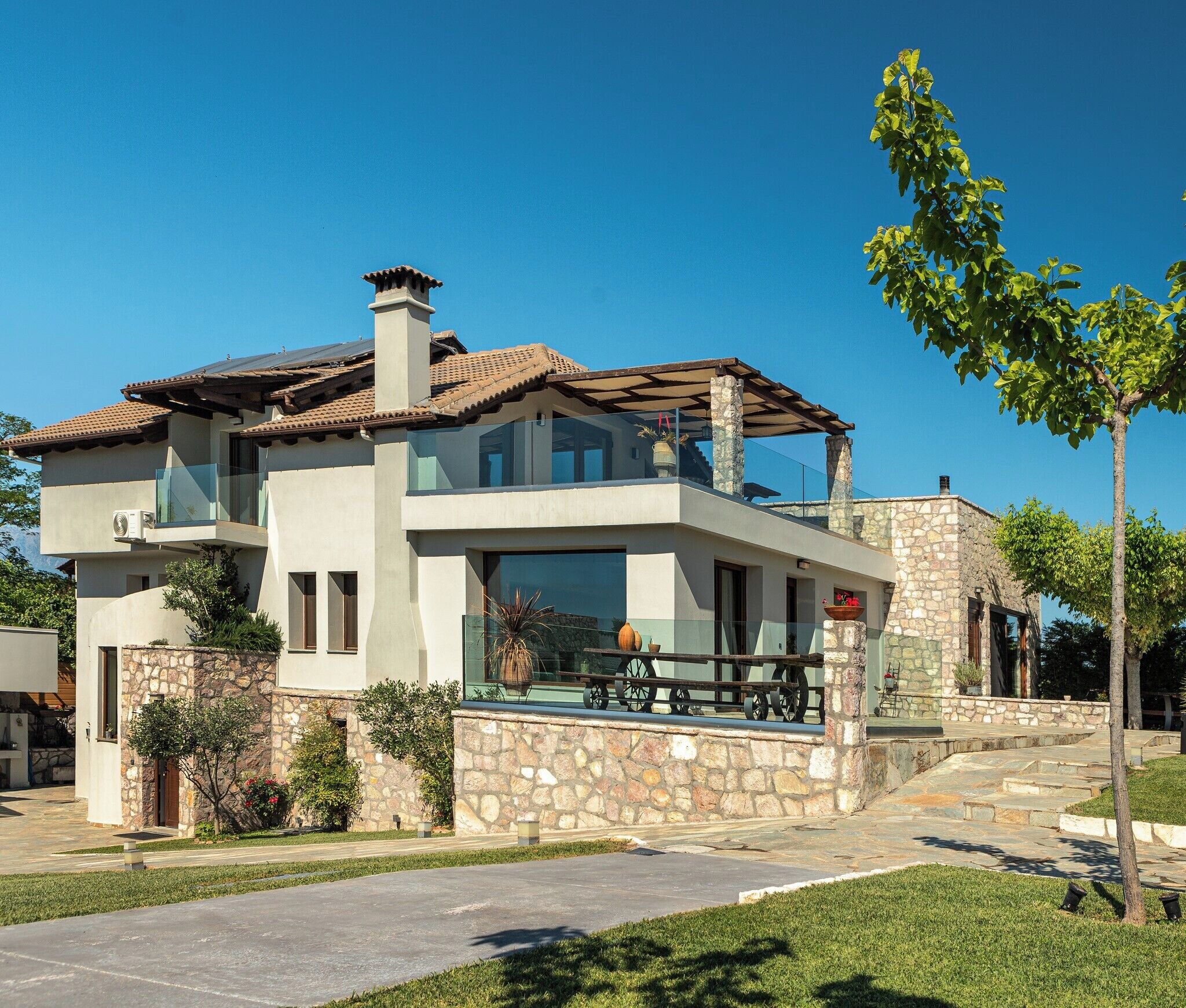 A modern two-story house with a stone facade, large windows, and a balcony with outdoor seating.