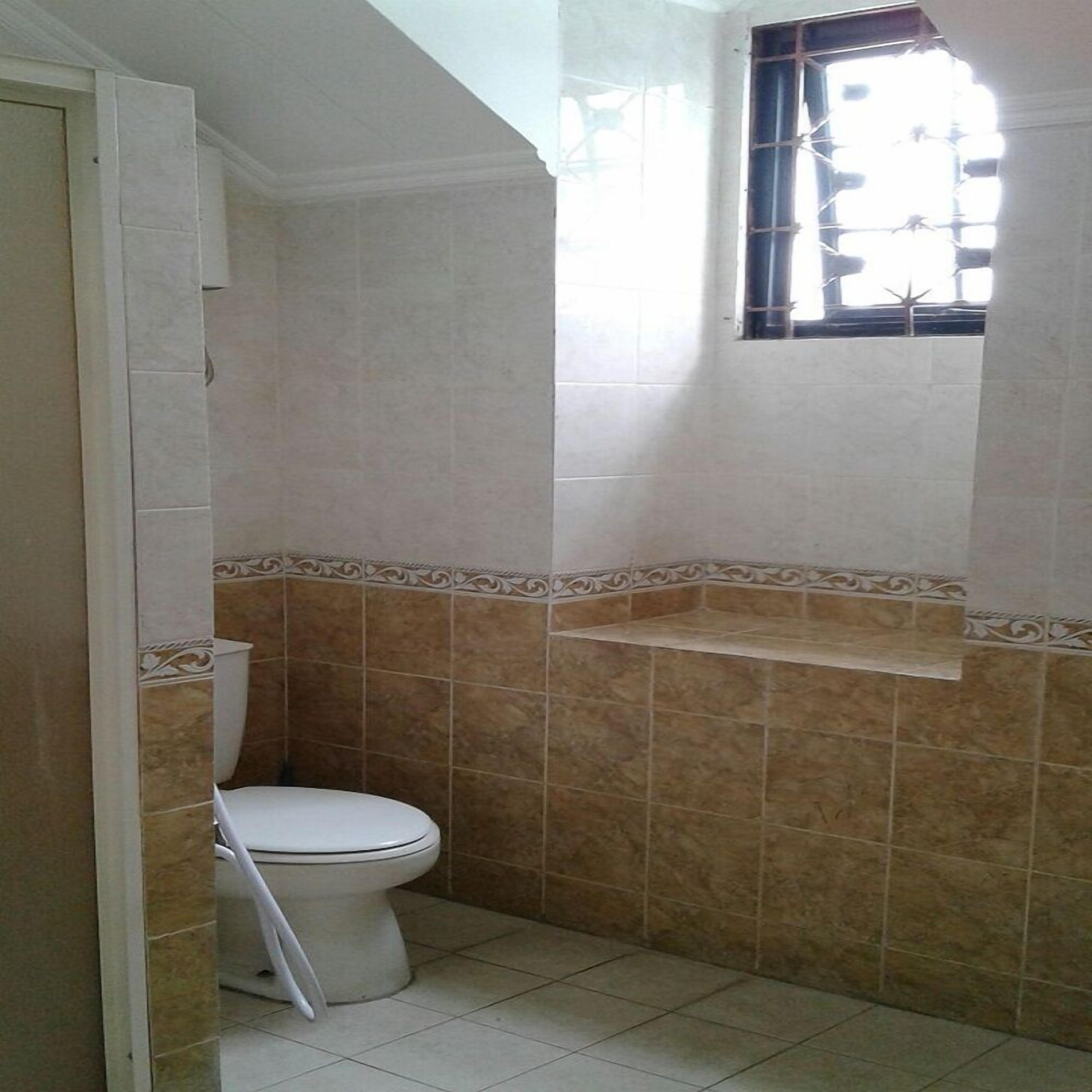 A small bathroom with a toilet, a window, and tiled walls.