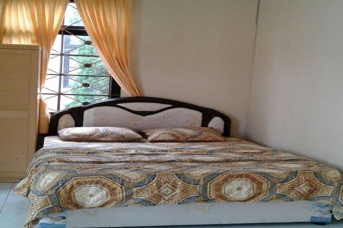 A bedroom with a bed, curtains, an air conditioning unit, and a window with a view of greenery.
