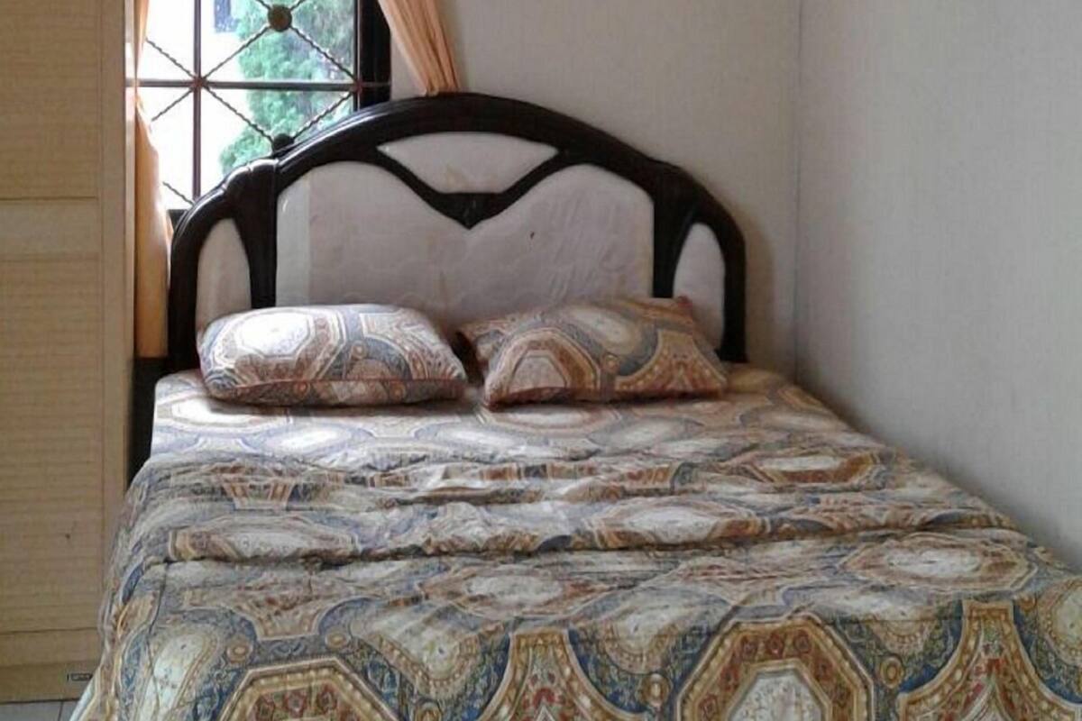 A bed with a patterned bedspread and two pillows, a window with curtains, and a tiled floor.