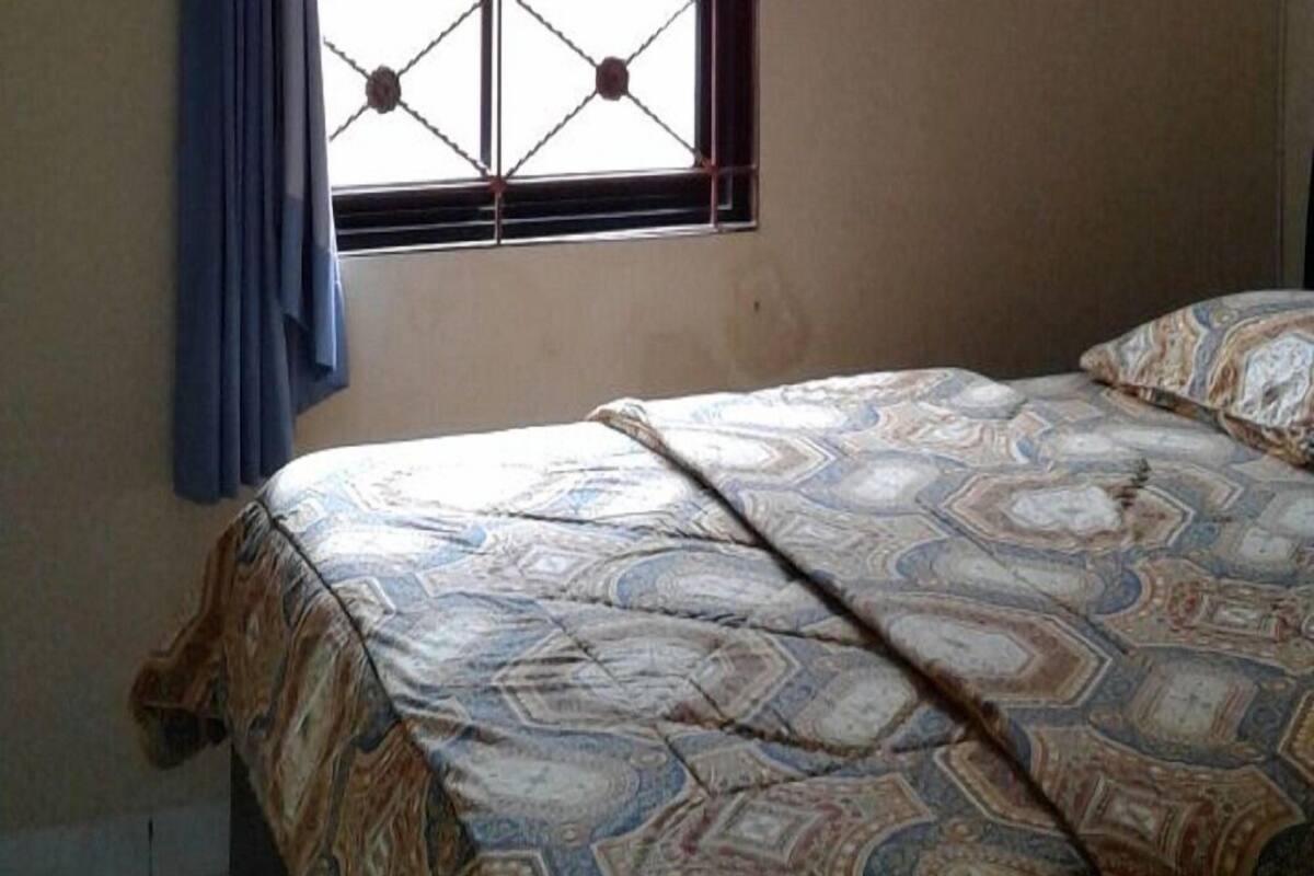 A bedroom with a bed, a window with curtains, and a tiled floor.