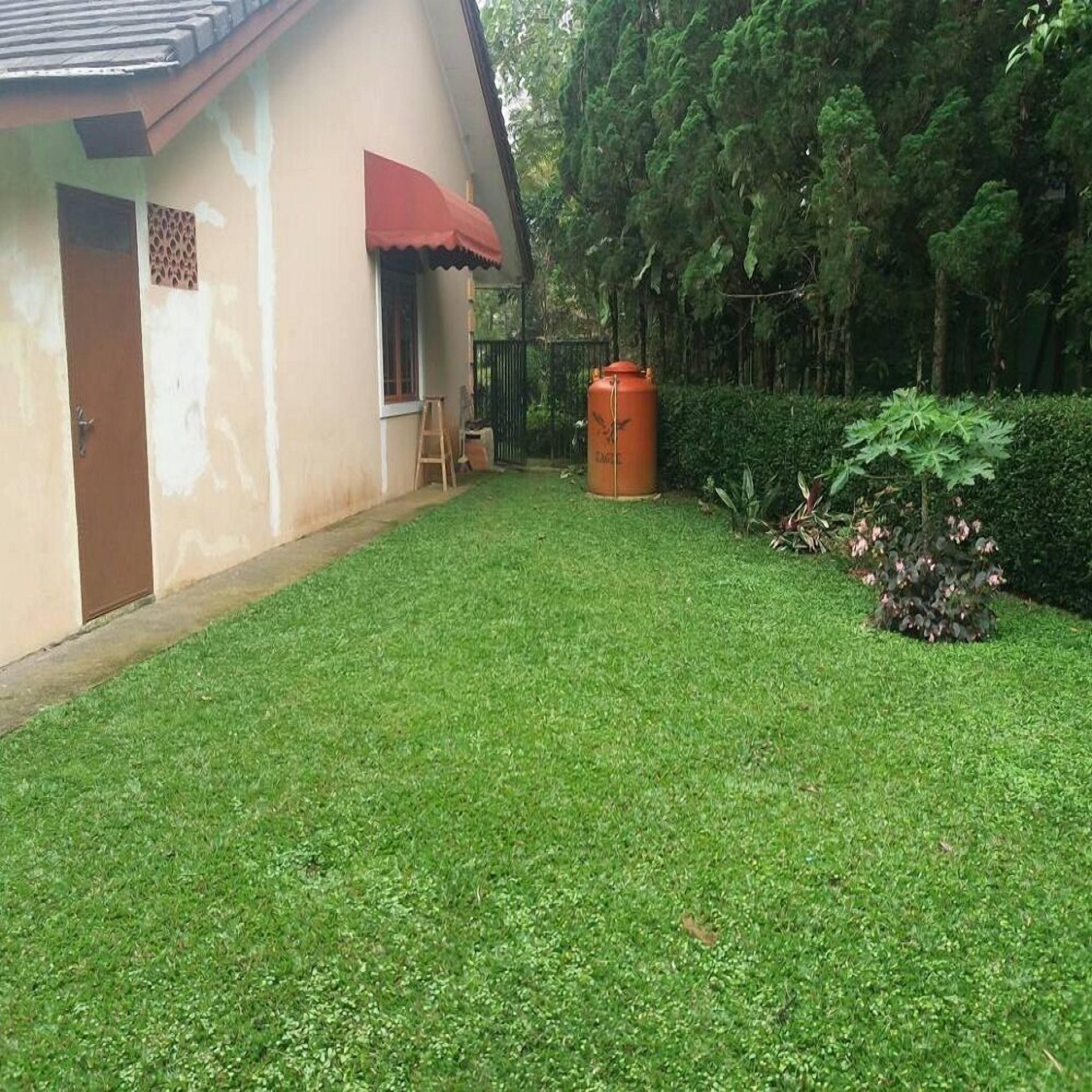 A house with a red awning, a large orange water tank, and a well-maintained lawn.