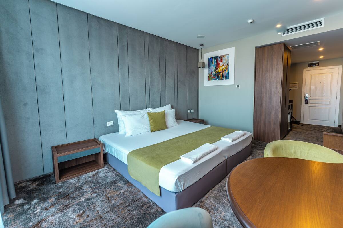 A hotel room with a bed, bedside table, and a small wooden bench.