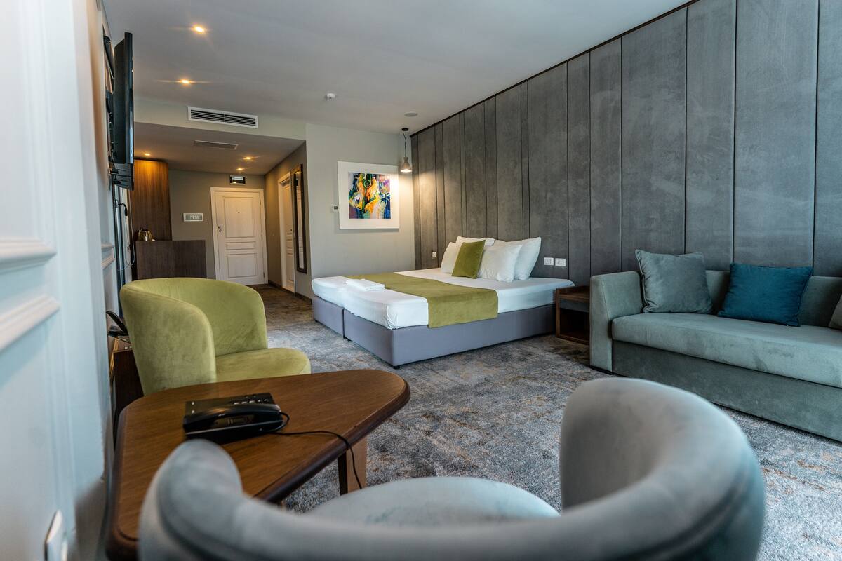 A modern hotel room with a bed, a sofa, a desk, and a chair.