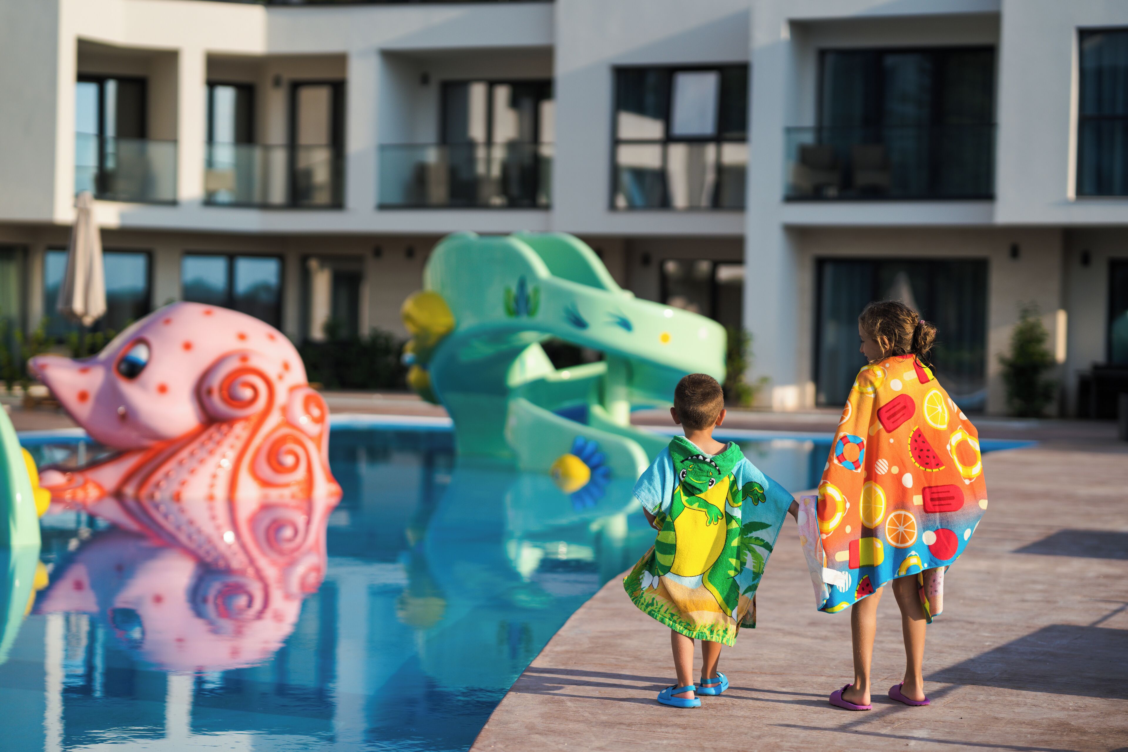 Two children walking by a pool with colorful octopus decorations.