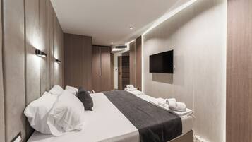A modern hotel room with a large bed, a flat-screen TV mounted on the wall, and a built-in air conditioning unit.