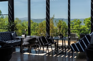 Uma área de estar moderna ao ar livre com vista para colinas verdes e montanhas.