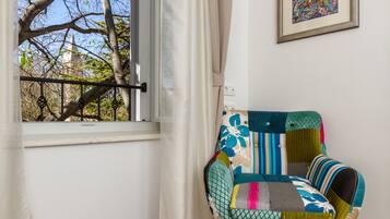 A room with a window, a colorful chair, and a framed picture on the wall.