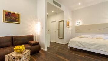 A modern bedroom with a bed, a brown leather sofa, a wooden side table with a bowl of lemons, and a painting on the wall.