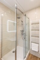 Ein modernes Badezimmer mit einer gläsernen Dusche, einem weißen Handtuchhalter und einem Fliesenboden.