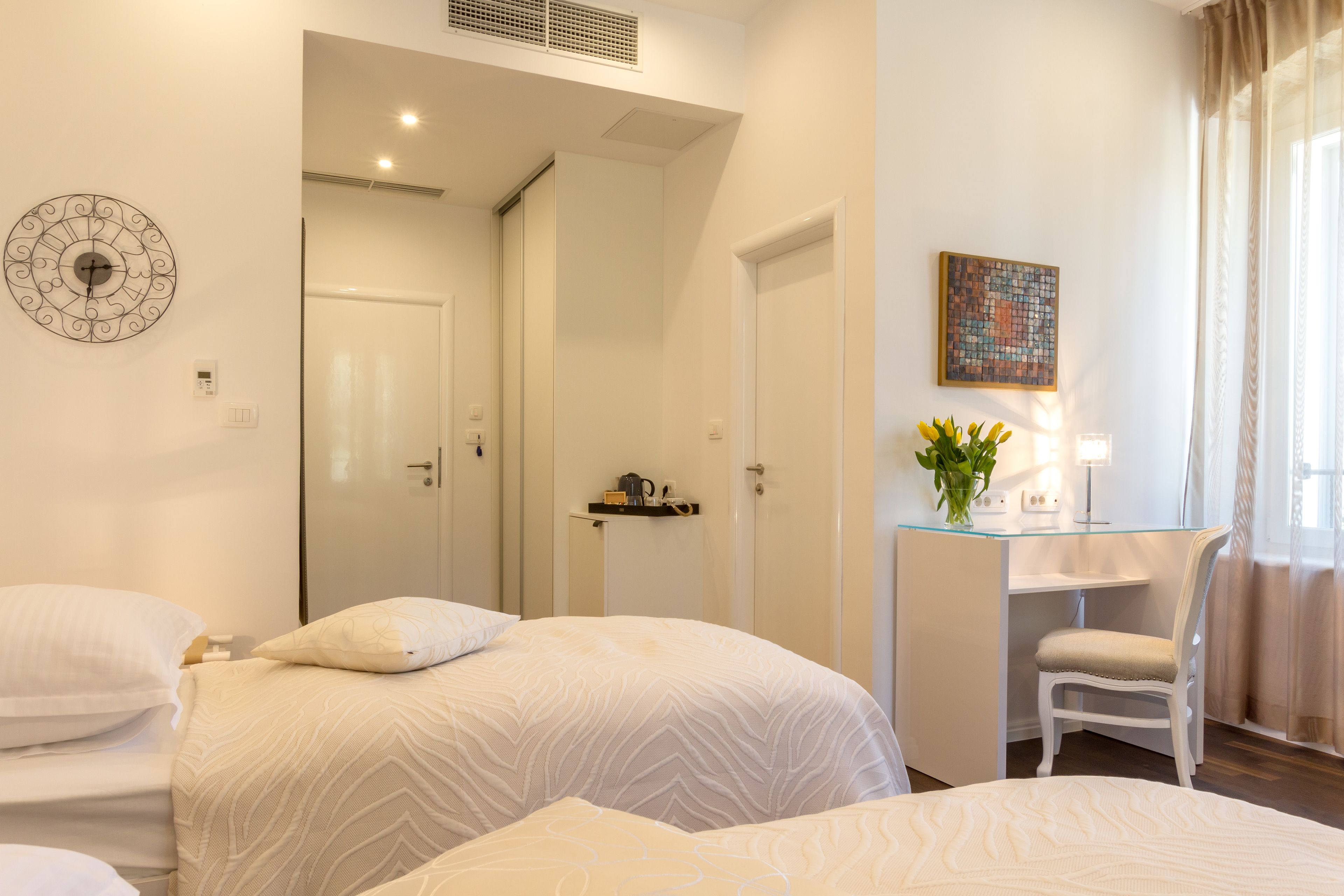 Une chambre d’hôtel avec deux lits, un bureau avec une chaise, une horloge au mur et un tableau.