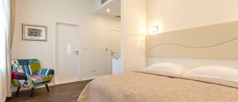 Un dormitorio con una cama, una silla de colores, una puerta y una lámpara fijada en la pared.
