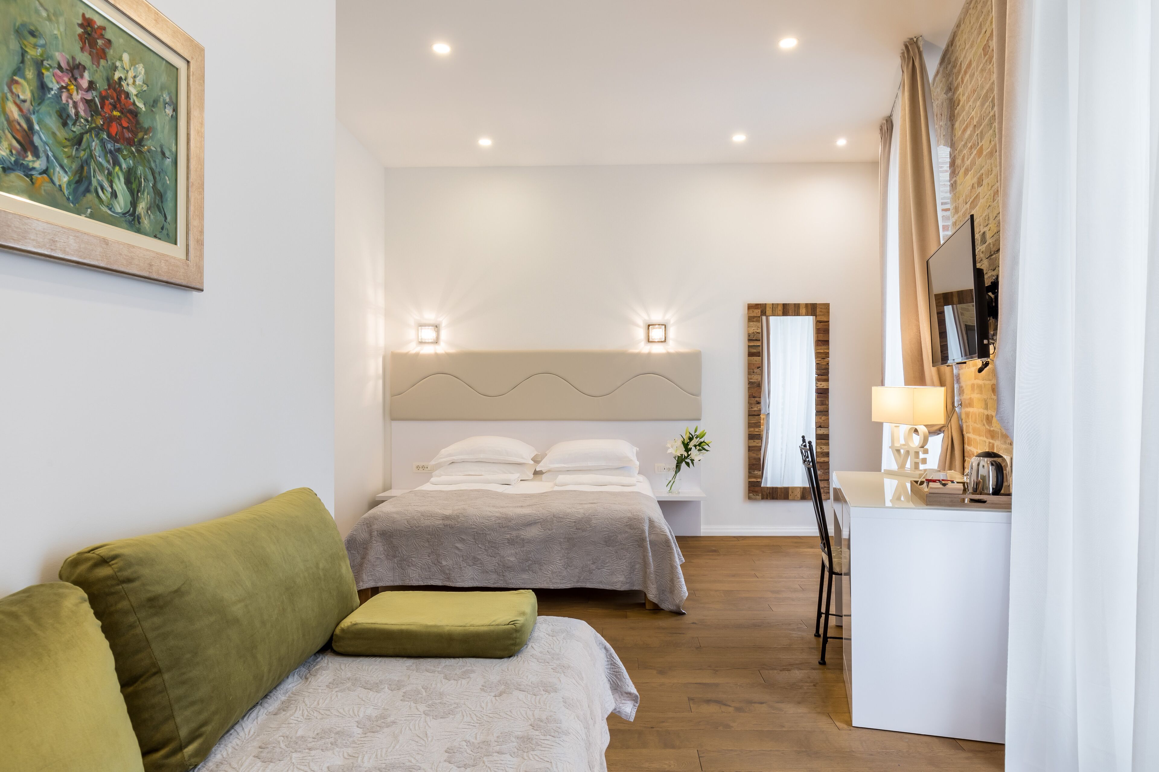 Una habitación de hotel moderna con una cama, un sofá, un escritorio con lámpara y un espejo.