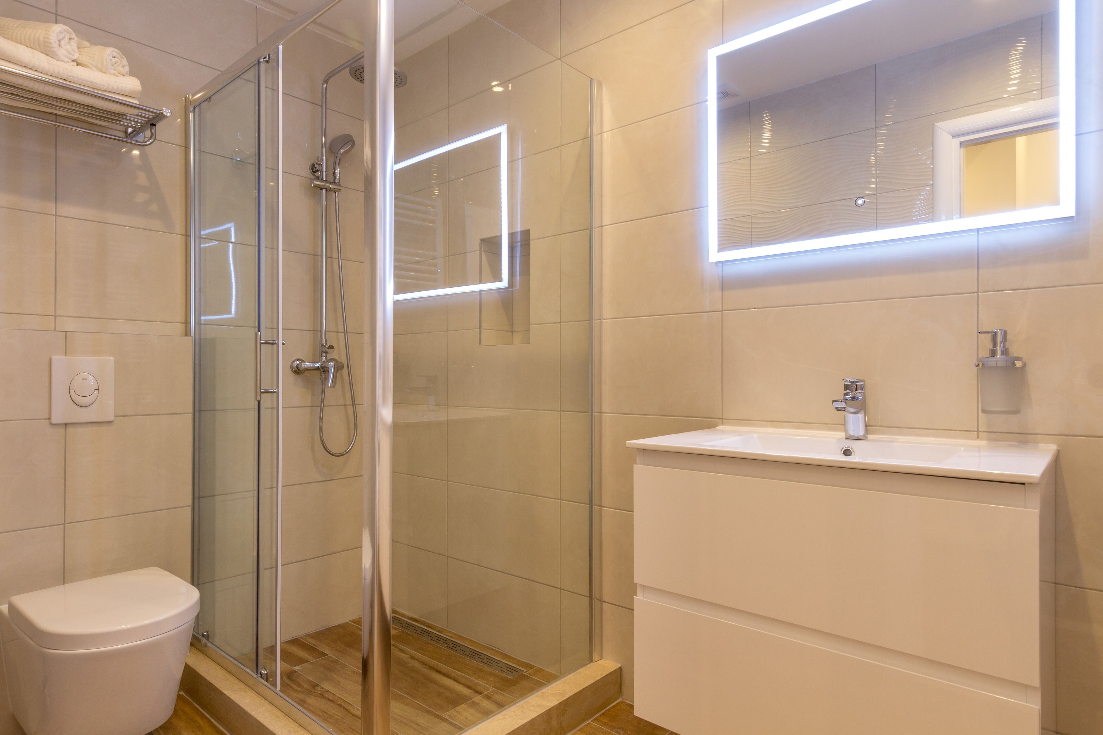 A modern bathroom with a glass-enclosed shower, a white sink, and a mirror with integrated lighting.