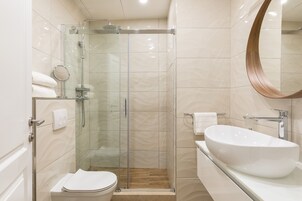 A modern bathroom with a glass-enclosed shower, a white sink, and a large mirror.