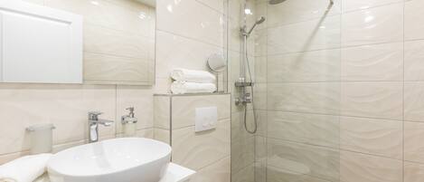 A modern bathroom with a large white sink, a toilet, a glass-enclosed shower, and a mirror.