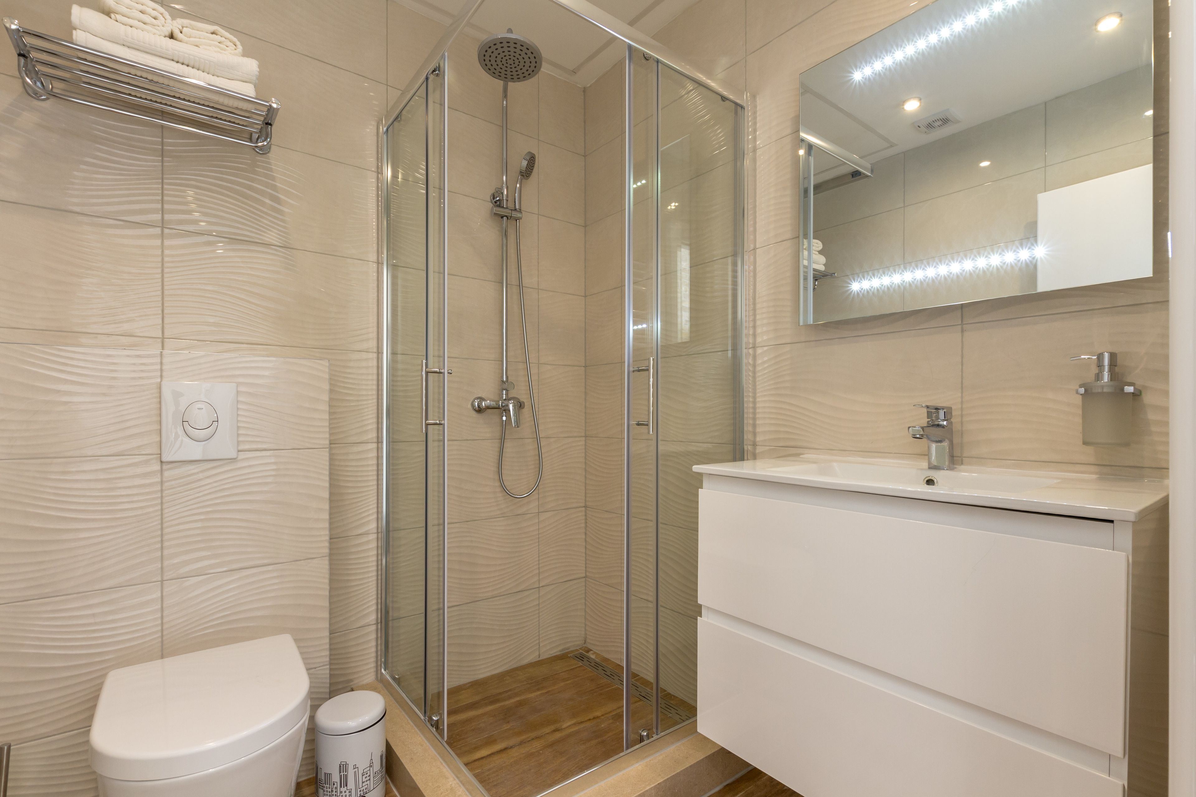 Une salle de bain moderne avec une douche à l’italienne, un lavabo blanc et un grand miroir.