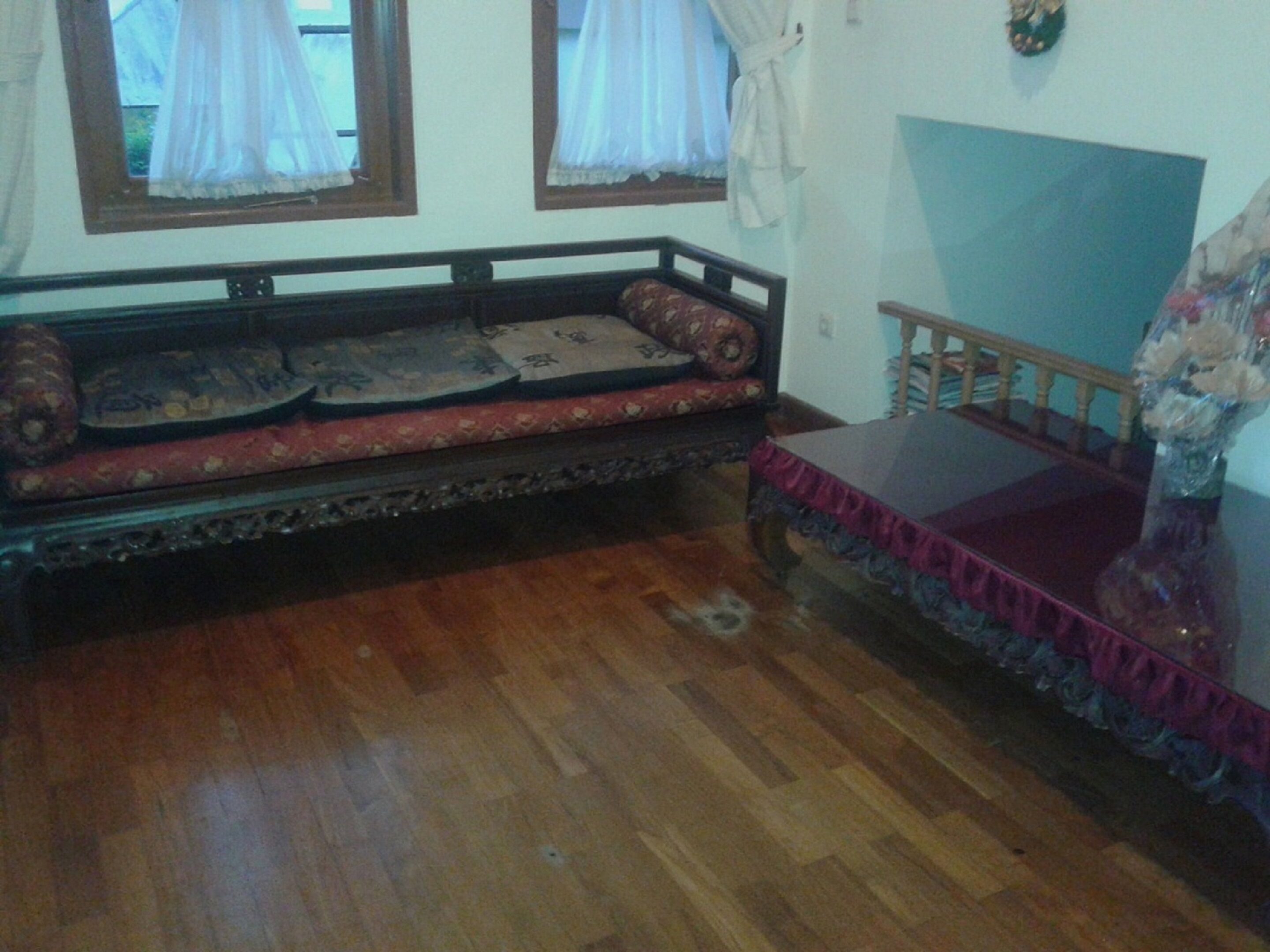 A room with a wooden floor, a sofa with patterned cushions, a small table, and a decorative wall hanging.