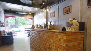 A reception area with a brick counter, framed pictures on the wall, and a view of the street outside. - Ok Chic Phuket Hostel (Phuket)