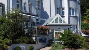 A two-story hotel with a red-tiled roof, a balcony with flower boxes, and a sign indicating the hotel name. - Hotelpension Vitalis (Bad Hersfeld)