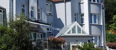 A two-story hotel with a red-tiled roof, a balcony with flower boxes, and a sign indicating the hotel name.