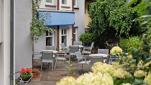 An outdoor seating area with multiple tables and chairs, surrounded by potted plants and flowers. - Hotelpension Vitalis (Bad Hersfeld)